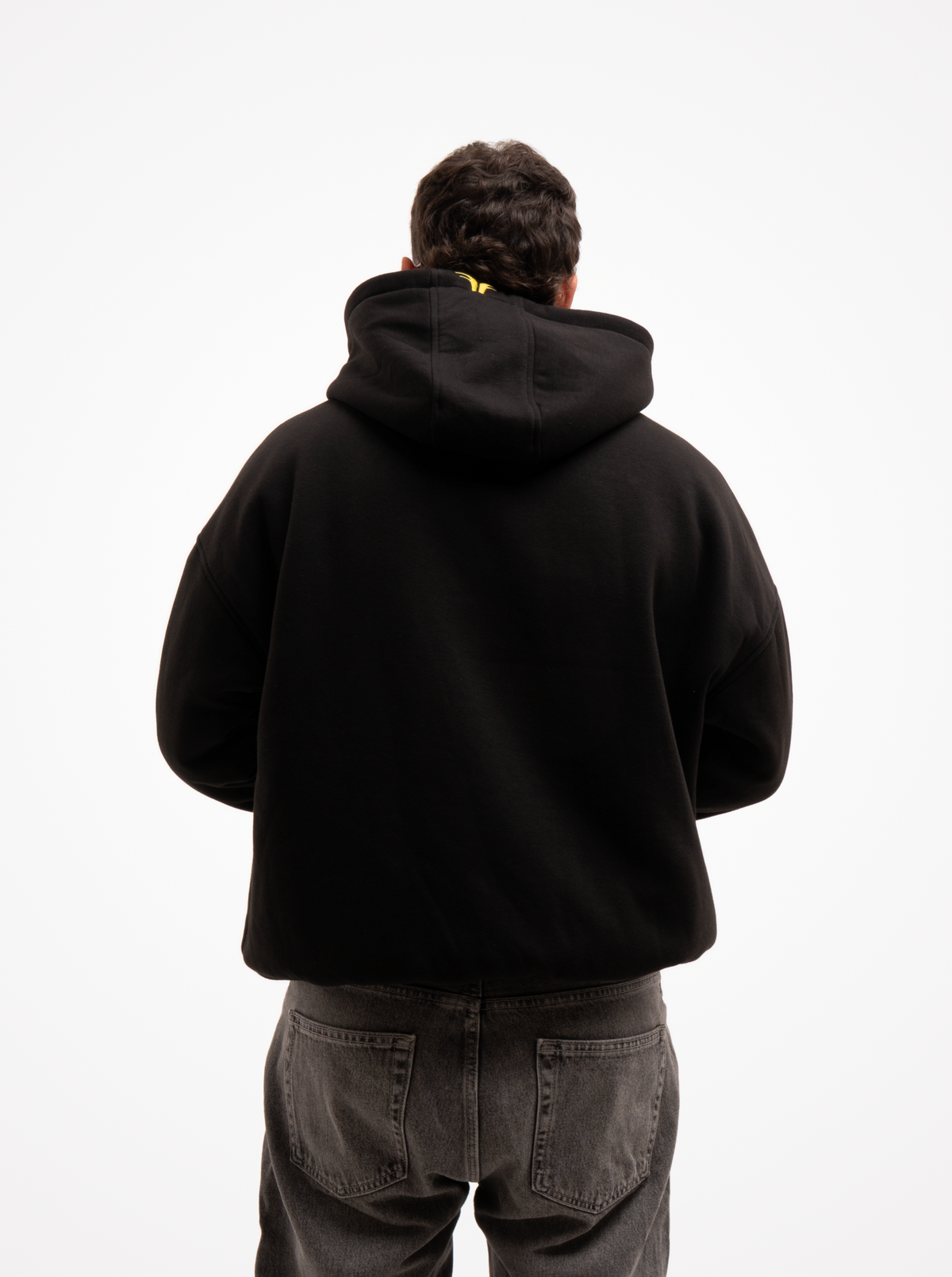 Hombre de espaldas con la sudadera de moto negra FORIDER, espalda lisa y pequeño logotipo amarillo en la capucha