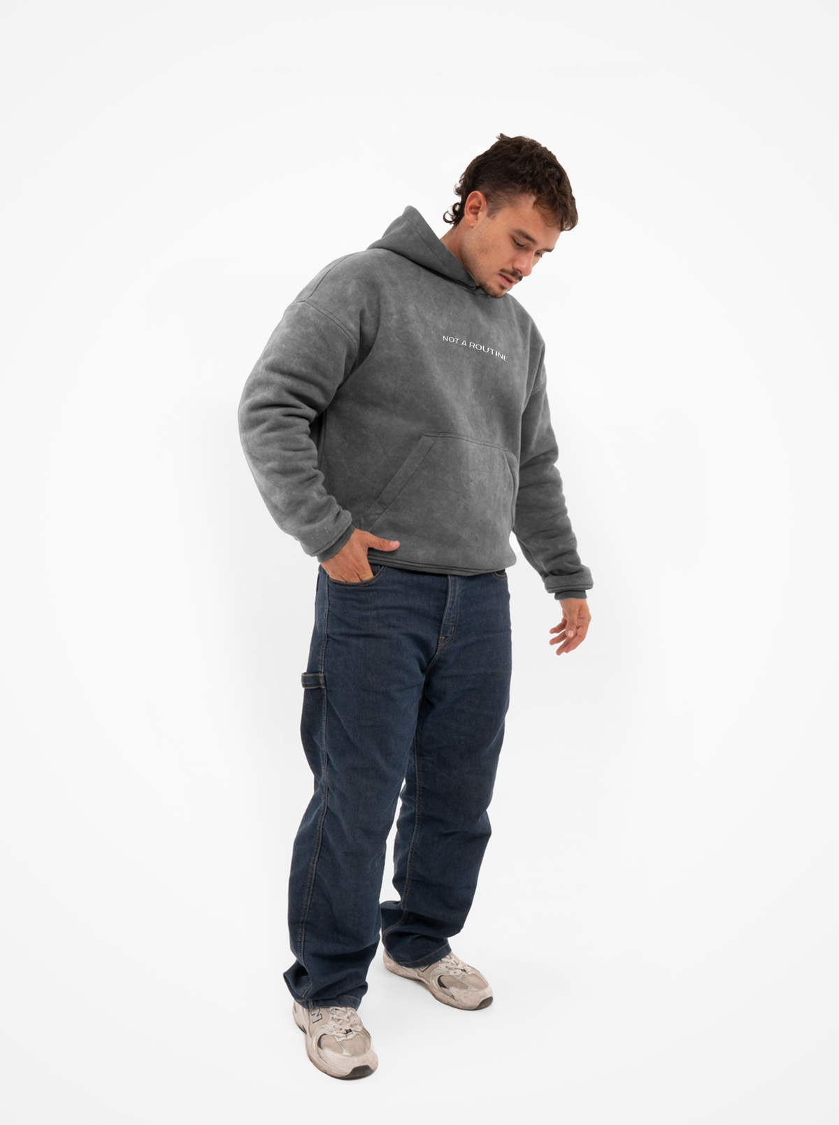 Hombre de cuerpo entero con la sudadera de moto gris washed, vaqueros y zapatillas, con una mano en el bolsillo