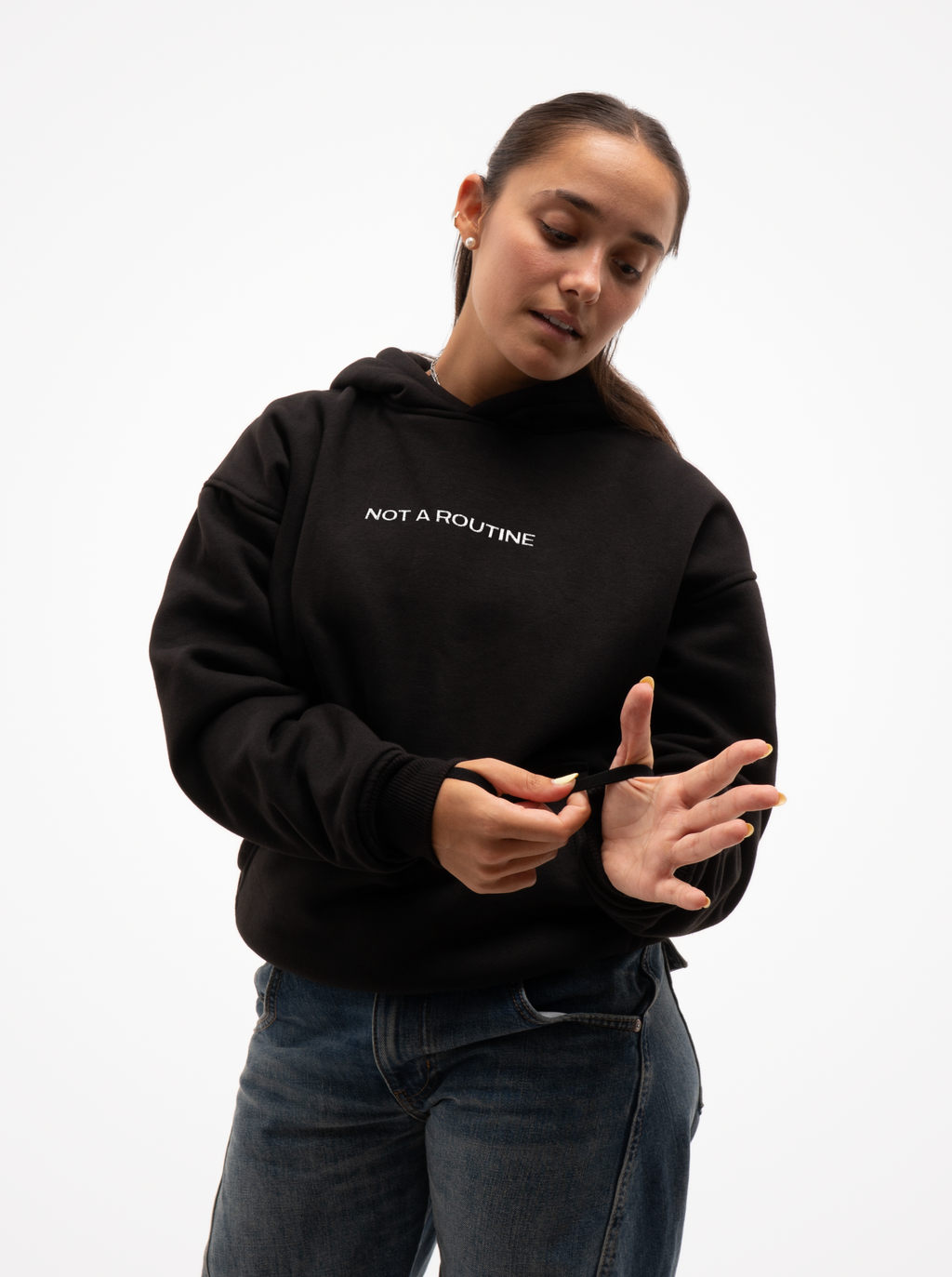 Mujer con la sudadera de moto negra Not a Routine vista de frente, ajustándose el puño de la manga, con vaqueros